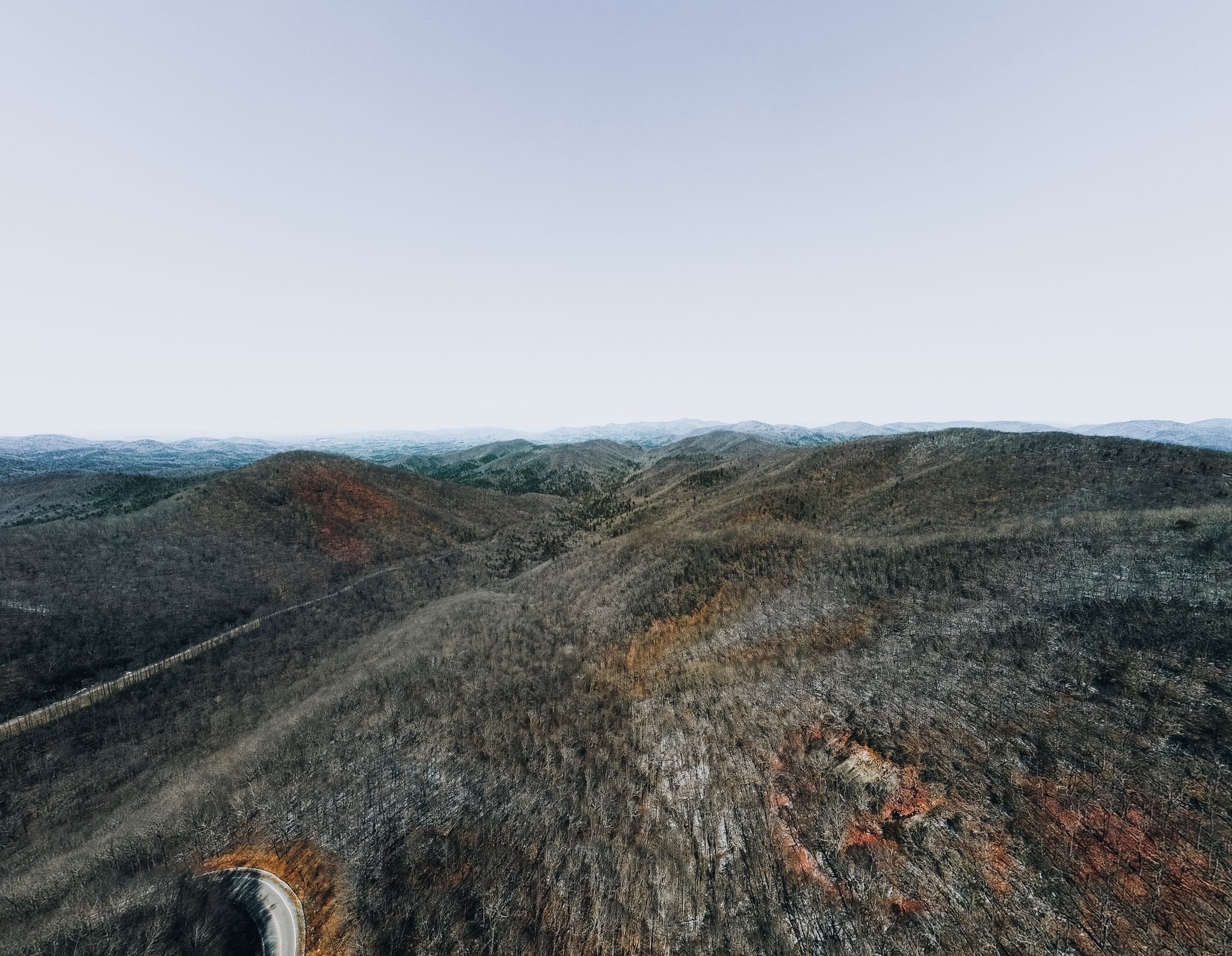 Drone shot of a tranquil mountain range with winding road and dense forest.