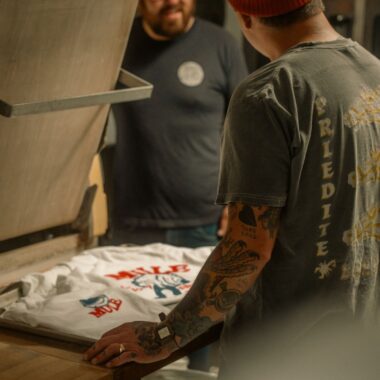 Two men engaged in screen printing a t-shirt in a cozy workshop setting.